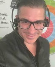Mann mit dunklen haaren, schwarzer Jacke, Brille und Headset auf dem Kopf.