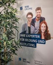 Ein Werbeaufsteller der WBS GRUPPE mit der Aufschrift Ihre Experten für Bildung und Recruiting.