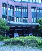 Ein rot gestrichenes Gebäude mit großen Fensterfronten. Vor dem Eingang steht ein Branchenwegweiser.