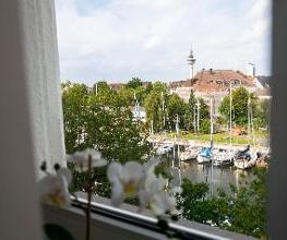 Blick aus dem Fenster am Standort. Ein Gewässer mit Segelbooten und vielen Bäumen.