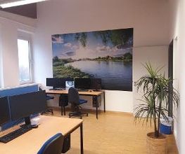 Ein Schulungsraum mit mehreren PC-Arbeitsplätzen. An der Wand hängt ein großes Bild eines Flusses.