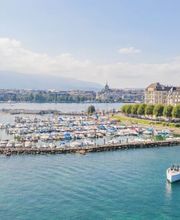 Panoramic view of Geneva’s waterfront with The Woodward hotel overlooking Lake Geneva and the Jet d’Eau fountain.