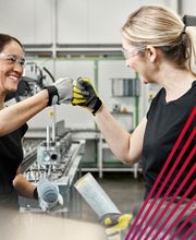 Zwei Mitarbeiterinnen von  actuell Personal arbeiten gemeinsam in einer modernen Produktionshalle. Mit Schutzbrillen, Arbeitshandschuhen und guter Stimmung zeigen sie Teamgeist, Zusammenarbeit und Freude an der Arbeit. Die Szene vermittelt ein positives Arbeitsumfeld in der Industrie und steht für Zusammenhalt, Motivation und professionelle Unterstützung im Arbeitsalltag.