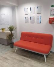 rotes Sofa, daneben ein Regal und Pflanzen. Über dem Sofa mehrere Plakate und ein Erste Hilfe Koffer und Instruktionen.