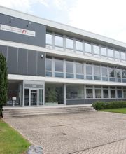 Im Hintergrund grau-weißes Bürogebäude, Fensterfront, im Vordergrund Beschilderung der Firmen des Gebäudes