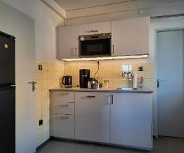 Küche mit mehreren Schränken, Wasserkocher, Kaffeemaschine und Kühlschrank.