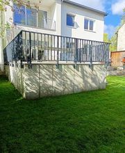 Neu gestalteter Garten mit sattgrüner Rasenfläche und einer erhöhten Terrasse am Wohnhaus. KK GaLaBau bei Berlin schafft funktionale Außenanlagen, die unterschiedliche Höhen harmonisch miteinander verbinden.