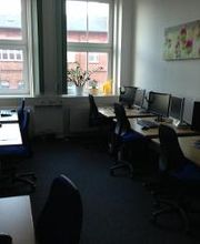 Schulungsraum mit mehreren Arbeitsplätzen mit jeweils 2 Bildschirmen, einem Bürostuhl, Tastatur, Maus und Headset.