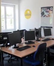 Schulungsraum mit 4 Arbeitsplätzen jeweils mit 2 Bildschirmen, einem Bürostuhl, Tastatur und Maus. An der Wand hängt ein Plakat.