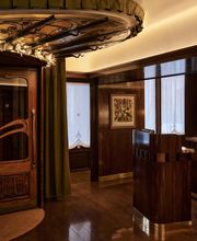 A polished dark wood host podium standing near an ornate Art Nouveau style wooden entryway topped with decorative stained glass lighting.