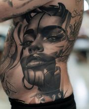 ein großes realistisches Tattoo auf den Rippen. Dargestellt ist ein Frauengesicht mit sehr ausdrucksstarken Augen.