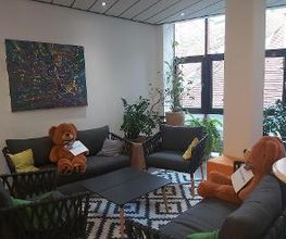 Aufenthaltsraum mit COuches, Sesseln und Tisch. auf den Couches liegen zwei Teddybären.
