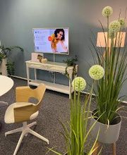 Aufenthaltsbereich mit mehreren Pflanzen. Vor der blauen Wand steht ein Regal mit TV, daneben eine Stehlampe.