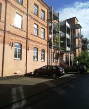 Backsteingebäude mit Balkonen und einem Parkplatz davor.