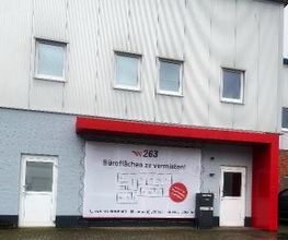 Außenansicht der Schulungsstätte mit Beschilderung der dort sitzenden Unternehmen. Graue Fassade und rote Überdachung,
