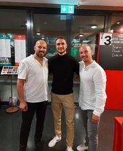 Drei Personen stehen gemeinsam in einem Innenbereich und posieren ruhig für ein Gruppenfoto. Die Szene wirkt strukturiert und vermittelt einen professionellen sowie persönlichen Austausch.
