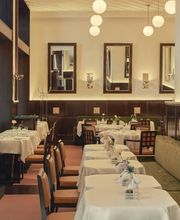 Elegant dining room with white tablecloths, green banquettes, and warm globe lighting.