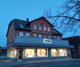 Modehaus Decker am Abend,
Die Schaufenster sind hell beleuchtet.