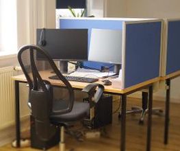 Typischer Teilnehmerarbeitsplatz mit einem schwarzen Bürostuhl und zwei Bildschirmen, Headset, Tastatur und Maus.