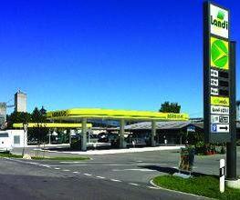 AGROLA Tankstelle in Lohn-Ammannsegg - Bätterkinden; Rechts Totem mit Landi Laden Logo, AGROLA Logo, digitaler Preisanzeige, selfwash; azurblauer Himmel; geschwungenes Dach mit drei Säulen
