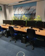 Schulungsraum mit mehreren PC-Arbeitsplätzen mit Monitor, Tastatur, Maus und Headset.