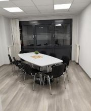 Ein Aufenthaltsraum mit weißem Tisch und mehreren schwarzen Stühlen.