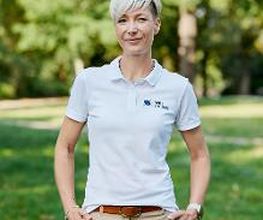 Eine Frau mit kurzen, blonden Haaren in beiger Hose und weißem Poloshirt.