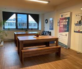 Pausenraum mit 32 Tischen und 4 Bänken. Hinten im Raum ein Sofa, daneben ein Roll Up Banner der WBS CODING SCHOOL.