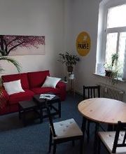 Aufenthaltsraum mit einem roten Sofa mit weißen Kissen, einem Tisch und mehreren Stühlen.