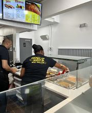 An employee at Golden Krust Kendall serving authentic jerk chicken, rice and peas, and steamed vegetables.