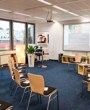 Schulungsraum mit Bestuhlung, an der Wand hängt eine Leinwand, auf die mit einem Beamer eine Präsentation geworfen wird.