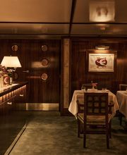 A intimate dining corner with a green carpeted floor, white-clothed table, dark wood paneled walls, and double doors with round porthole-style windows.