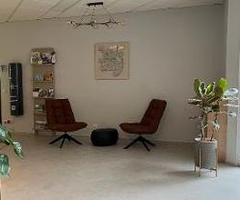 Foyer mit gemütlicher Sitzgruppe bestehend aus zwei dunkelroten Sesseln, einem Sitzkissen und einem Bild an der Wand. Daneben ein Regal sowie einige grüne Zimmerpflanzen.