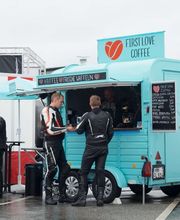 FirstLoveCoffee GmbH - Kaffee Catering Berlin - Türkiser Kaffeeanhänger auf Veranstaltungsgelände mit Gästen, Kaffeespezialitäten, frischen Waffeln und mobiler Barista-Bar für Events und Messen.