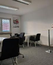 Pausenraum mit zwei Tischen, vier Sesseln und einem Stehtisch auf dem eine Topfpflanze steht.