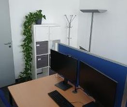 Schreibtisch im Trainingsraum mit zwei Bildschirmen, Tastatur und Maus. An der Wand steht ein Regal mit Pflanze