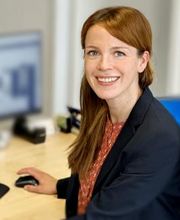 Portrait von Mandy Altmann, Teamassistentin am WBS Standort Güstrow. Sie hat lange, hellbraune Haare und sitzt am Schreibtisch vor ihrem Computer und lacht fröhlich in die Kamera.
