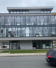 mediaService Bremen | Full-Stack Werbeagentur - Die Außenansicht eines modernen, dreistöckigen Bürogebäudes mit einer großen Glasfassade und davor geparkten Fahrzeugen an einer Straße.