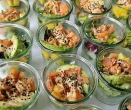 dean&david Catering | Pforzheim - Nahaufnahme von Lachs Bowls im Glas mit Avocado, Mango, Salat, Sesam und cremigem Dressing als frische Bowl-Auswahl für Events.