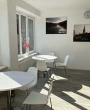 Ein heller Aufenthaltsraum mit runden, weißen Tischen, passenden Stühlen und Leinwandbildern von Hamburg an der Wand.