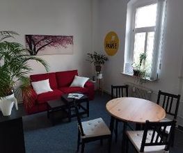 Aufenthaltsraum mit einem roten Sofa mit weißen Kissen, einem Tisch und mehreren Stühlen.