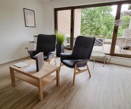 Zwei gemütliche Sessel mit Tisch im Pausenraum mit Blick auf die Terrasse mit Gartenmöbeln.