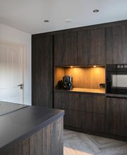 KH System keuken, frontkleur Cleaf Sherwood donker, werkblad keramiek Nero Satin, bargedeelte in de kleur Rustiek Eiken. Kookplaat met geïntegreerde afzuiging.