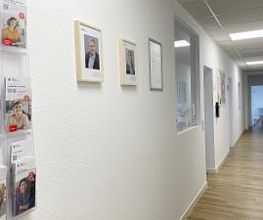 Langer Flurbereich mit Flyerständer und Bildern an der Wand.