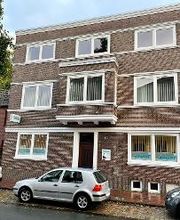 Ein Backsteinhaus mit drei Etagen. Davor sind 3 Autos geparkt