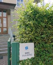Logo von WBS TRAINING am Eingang in der Hecke, im Hintergrund die Treppe und die Eingangstür.
