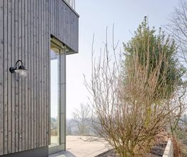 Detailansicht des modernen Anbaus mit vertikaler Holzverschalung, großzügiger Glasfassade und klar gegliederter Außenanlage. Architektur und Landschaftsgestaltung greifen harmonisch ineinander.