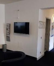 Empfangsbereich und Flur mit Sesseln und einem TV. Daneben hängt ein Flyerhalter.