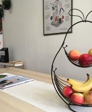 Gemütliche Küche/Aufenthaltsbereich. Heller Holztisch mit Zeitschriften und einer großen Obstschale mit frischem Obst. An den Wänden Bilder, im Hintergrund ein Aufsteller.