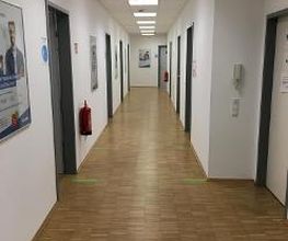 Ein langer Flur mit Holzboden. Links und rechts gehen mehrere Türen ab.